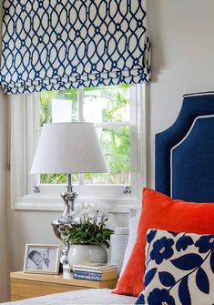 a bedroom with blue and white bedding, orange pillows and a lamp on the nightstand