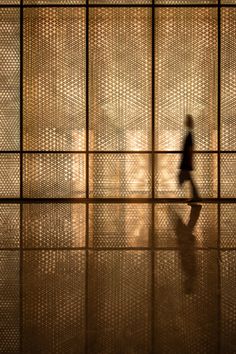 a person walking in front of a wall with many squares on it and the light shining through