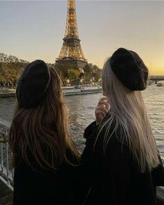 two women standing next to each other in front of the eiffel tower at sunset