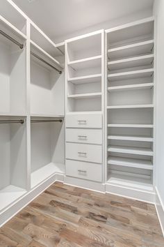 an empty walk in closet with white shelves and drawers on the wall, along with wooden flooring