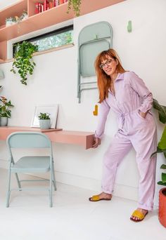 a woman standing next to a shelf with plants on it and a chair in the background