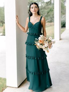 a woman in a green dress standing next to a white column and holding a bouquet