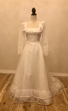 a white wedding dress is displayed on a mannequin headdress in front of a wall