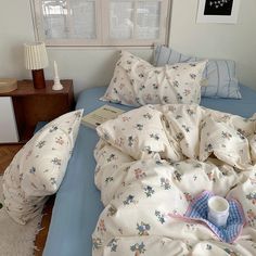 an unmade bed with blue sheets and white pillows on it, next to a night stand