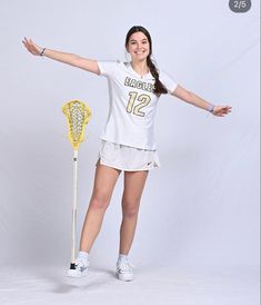 a woman in white shirt and shorts holding a lacrosse racquet next to a yellow stick