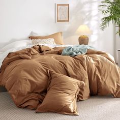 a bed with brown sheets and pillows in a room next to a potted plant