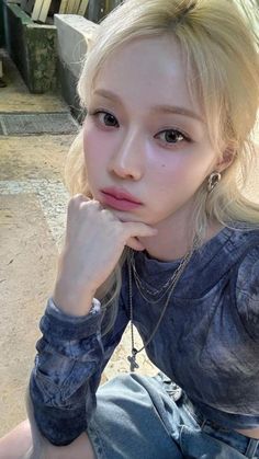 a young woman sitting on the ground with her hand under her chin and looking at the camera