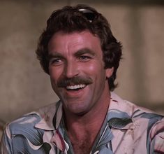 a man with a moustache smiling at the camera while wearing a hawaiian shirt