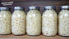 four jars filled with white onions sitting on top of a wooden shelf next to each other