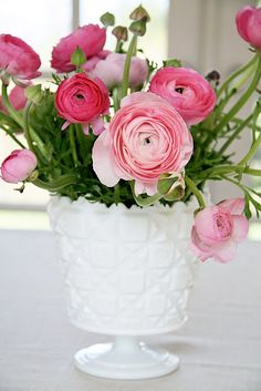 a white vase filled with pink flowers on top of a table