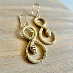 Embrace timeless elegance with our Infinity Snake Earrings, meticulously crafted from golden brass to captivate with their intricate infinity symbol shaped snake design. Each pair is handcrafted with meticulous attention to detail, showcasing the graceful curves and intricate patterns that define the snake motif. The golden brass adds a touch of warmth and sophistication, making these earrings a versatile choice for both everyday wear and special occasions. Material: High quality brass Width: Approx 3/4 inch (2cm) Length: Approx 2 3/4 inches (6.98cm) ** Caring for Brass jewelry ** - Using a toothbrush and toothpaste, brush the brass gently for a couple of minutes and rinse. - Or using a brass polishing cloth - they work great and last for a very long time.   Handcrafted Disclosure  All pie Symbolic Snake-shaped Brass Jewelry, Bronze Snake Shape Jewelry As Gift, Bronze Snake-shaped Jewelry Gift, Bronze Snake-shaped Jewelry For Gift, Elegant Snake-shaped Metal Jewelry, Elegant Handmade Snake-shaped Jewelry, Elegant Snake Shape Earrings With Ear Wire, Symbolic Gold Snake Jewelry, Gold Infinity Shaped Metal Jewelry