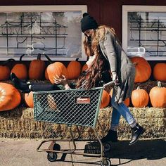 a woman pushing a shopping cart full of pumpkins