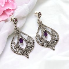 For sale are these gorgeous earrings set in solid silver; they have two sparkling amethyst gemstones. Marcasite gemstones surround the earrings.  The back is hallmarked with '925' to show that they have been made with sterling silver.  Great as a gift or adding a little something extra to an outfit looks great against any skin tone. Wear them with swept-back hair to show it off. This captivating pair arrives in a beautifully presented gift box, adding an extra touch of sophistication to your jew Swept Back Hair, Outfit Looks, Purple Gift, British Countryside, Silver Dangle Earrings, February Birthstone, February Birth Stone, Silver Earrings Dangle, Amethyst Gemstone