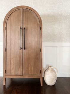 a wooden cabinet sitting next to a white vase on top of a hard wood floor