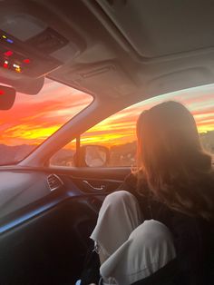 a woman sitting in the driver's seat of a car as the sun sets