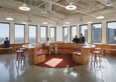 people are sitting on benches in an office with large windows and floor to ceiling windows