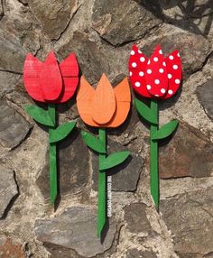 three wooden flowers with polka dots on them sitting next to a stone wall, one red and one orange