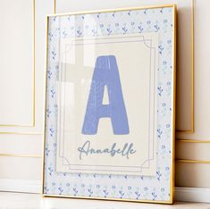 a blue and white framed letter sitting on top of a wooden floor next to a wall