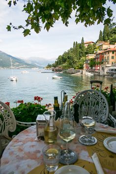 an outdoor dining table with wine glasses and plates on it overlooking the water's edge