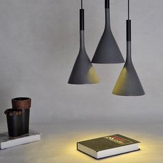 three pendant lights hanging from the ceiling above books and a cup on a table next to a candle