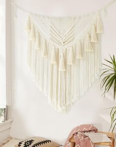 a white wall hanging with tassels in a room next to a potted plant