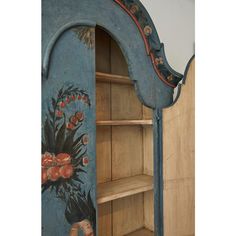 an old blue painted bookcase with flowers and leaves on the front, next to a wooden shelf