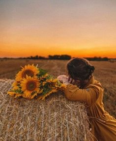 a woman standing on top of a bale of hay next to a sunflower