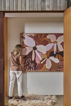 a woman standing in front of a painting on the side of a wall next to a rug