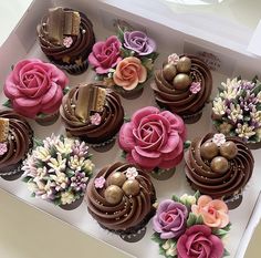 a box filled with lots of cupcakes covered in chocolate frosting and flowers