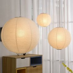 three white paper lanterns hanging from the ceiling above a cabinet and sideboard in a living room