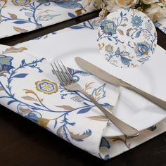 a place setting with white and blue floral napkins, silverware and flowers on the table