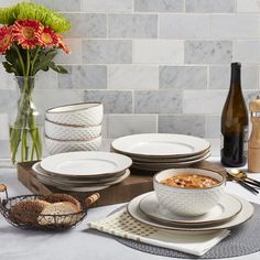 the table is set with plates, bowls and wine bottles in front of a vase filled with flowers