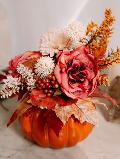 a vase filled with flowers and leaves on top of a marble countertop in front of a white wall