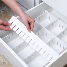 a person is opening the bottom drawer of a kitchen cabinet with white plastic dividers