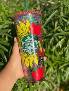 a hand holding a starbucks cup with an apple and sunflower design on the side