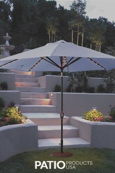 a white umbrella sitting on top of a lush green field next to steps and trees