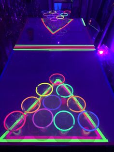 an illuminated table with neon circles and glasses on the top, in a dark room