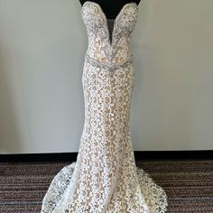 the back of a wedding dress on display in front of a white wall and black mannequin