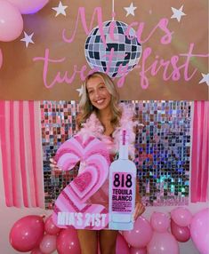 a woman holding a bottle in front of balloons and a sign that says miss first