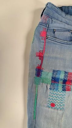 an old pair of jeans with colorful stitching on the bottom and side, sitting against a white wall