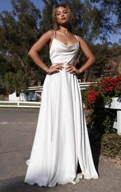 a woman in a long white dress standing on the street with her hands on her hips