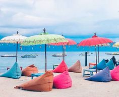 colorful beach chairs and umbrellas are on the sand near the water with boats in the background