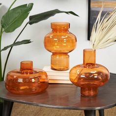 three orange vases sitting on top of a wooden table next to a green plant