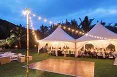 a dance floor is set up in the middle of a lawn with white tents and string lights