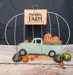 an old blue truck with pumpkins and hay in the back sits on a wooden table