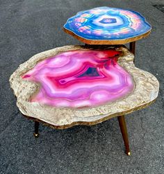 two tables with colorful designs on them sitting in the middle of a parking lot next to each other