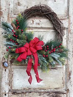 a wreath with red berries, pine cones and greenery hangs on an old door