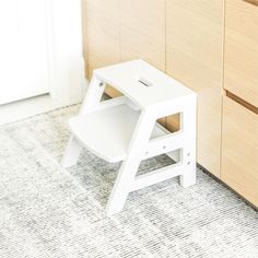 a small white step stool sitting next to a wooden cabinet in a room with carpet