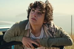 a young man leaning on the hood of a car