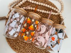 four glass tumblers with halloween designs on them sitting next to a bead necklace